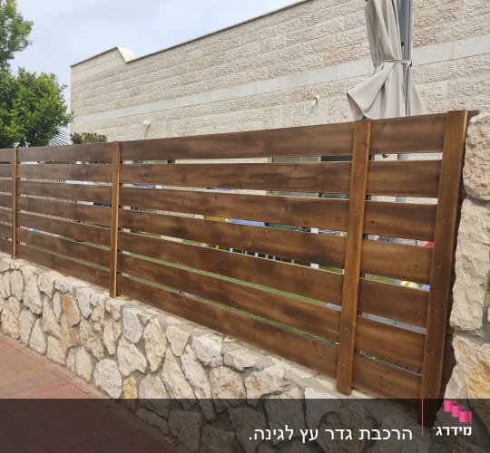 גדר עץ חומה על קיר אבן בגינה